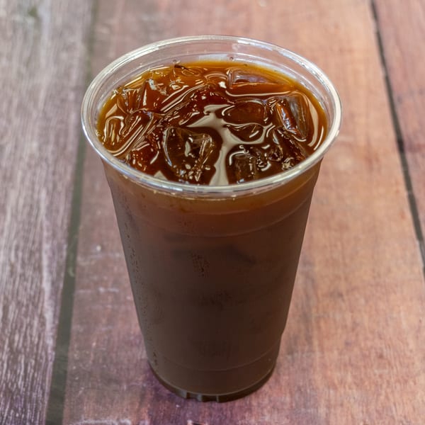 Iced coffee in a clear plastic cup with ice cubes, on a wooden surface.