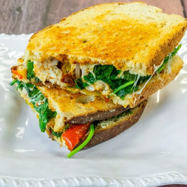 Toasted sandwich with melted cheese, spinach, and red peppers, cut in half on a white plate.