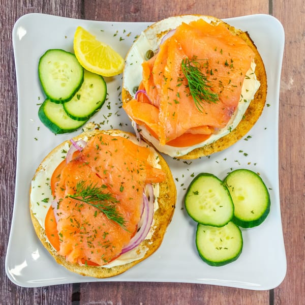 Two Chelsea Coffee Company bagels with smoked salmon, cream cheese, tomato, onion, and dill, served with cucumber and lemon.