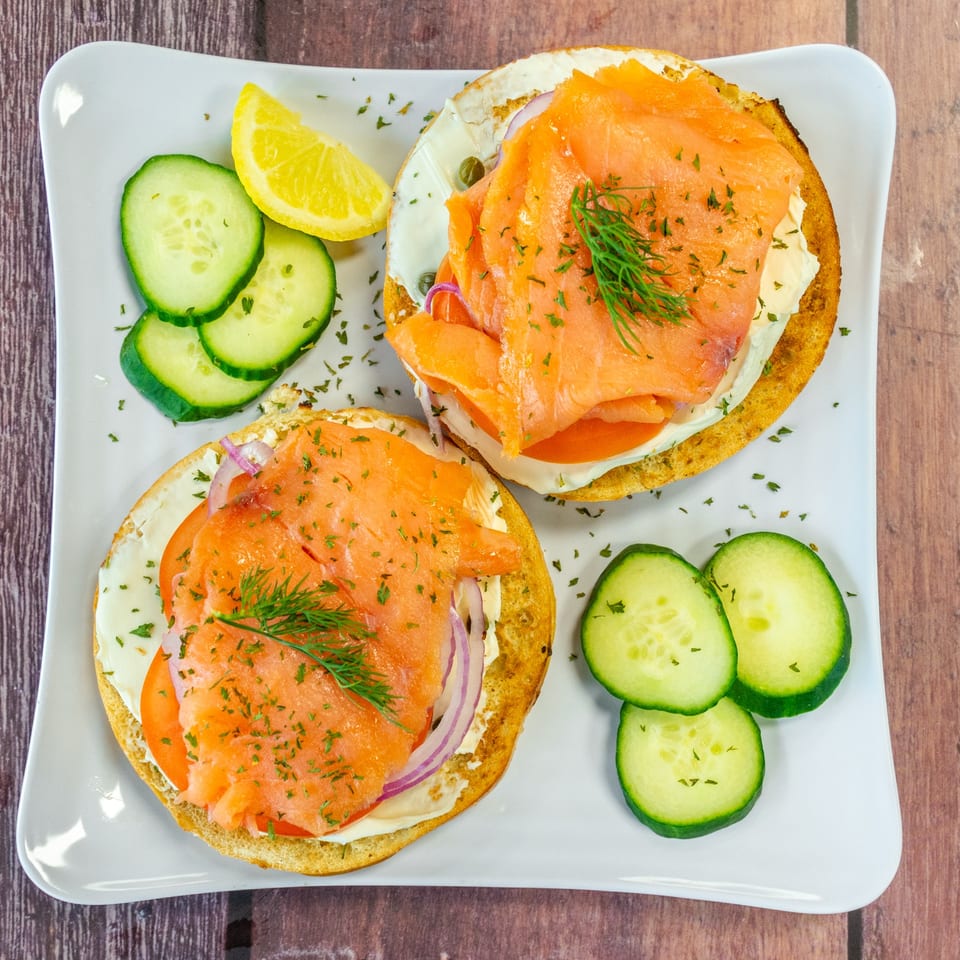 Two Chelsea Coffee Company bagels with smoked salmon, cream cheese, tomato, onion, and dill, served with cucumber and lemon.