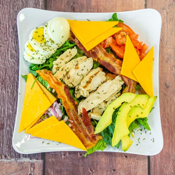A Cobb salad with chicken, bacon, avocado, hard-boiled eggs, cheese, and tomatoes on a white plate.
