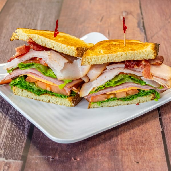 A Chelsea Coffee Company club sandwich, cut in half, with turkey, bacon, lettuce, tomato, and cheese.