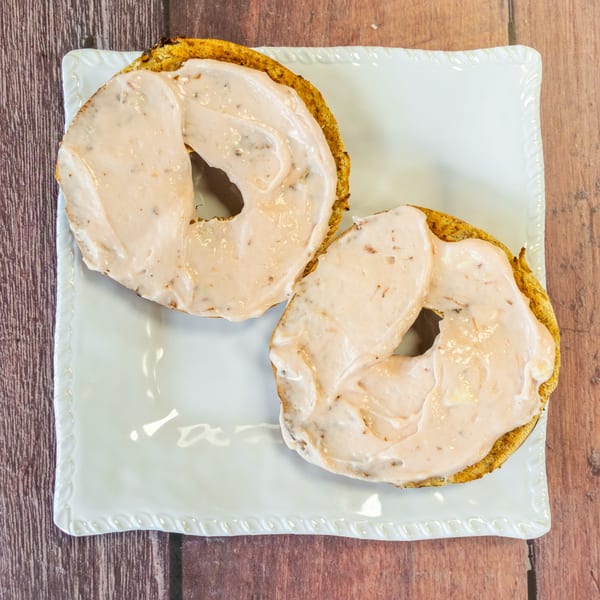 Two toasted bagels with cream cheese on a white rectangular plate on a wooden table.
